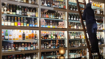 Jason on a ladder admiring bottles of Scotch stacked to the ceiling