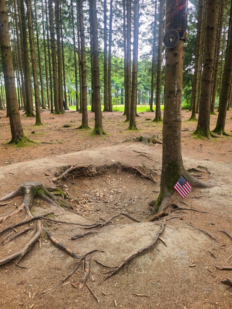 A foxhole with a tiny American flag in the Ardennes Forest