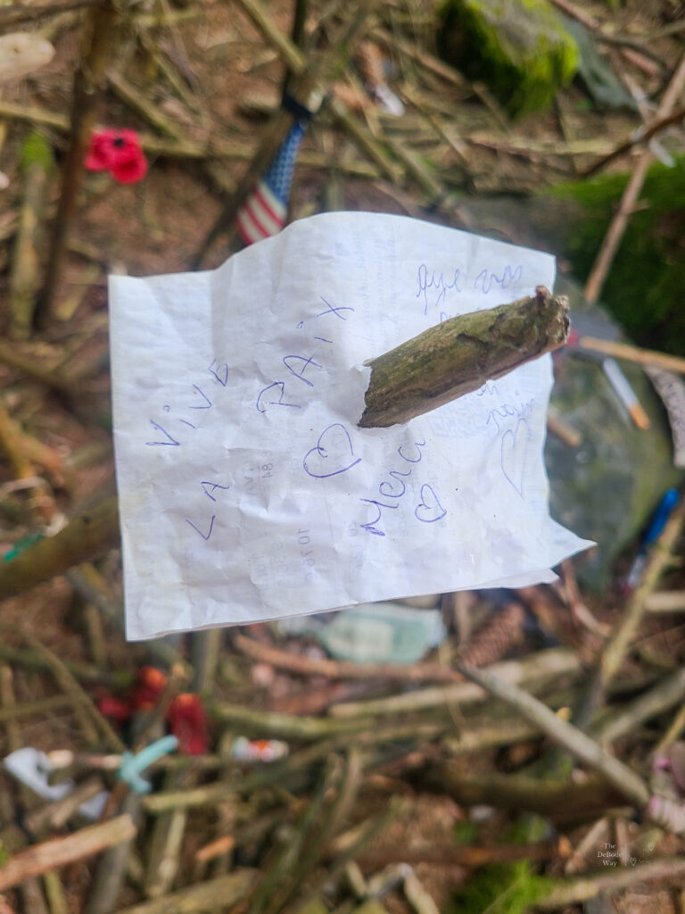 A white piece of paper stuck on the top of a cross that reads "Viva la paix, Merci"