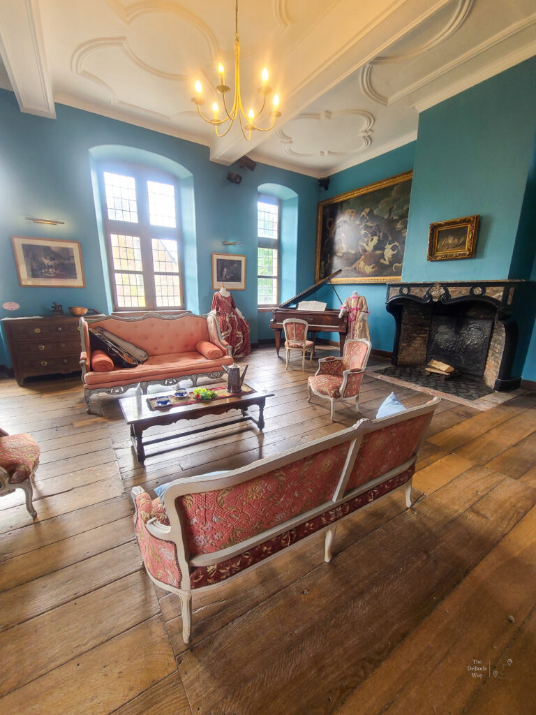 The music room arranged with pink furniture, a piano, and blue walls at Chateau de Lavaux-Sainte-Anne