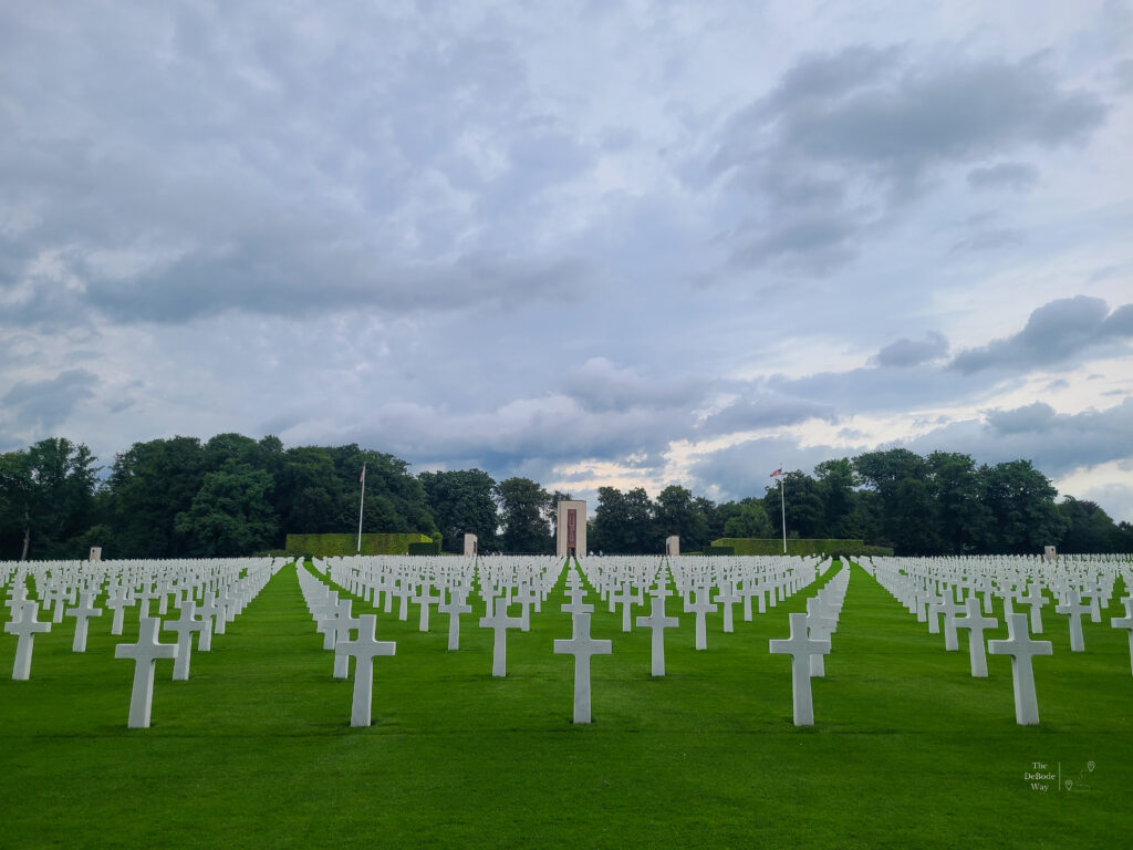 White crosses in neat rows in green grass with a cloudy, dreary sky above at the Luxembourg American Cemetery
