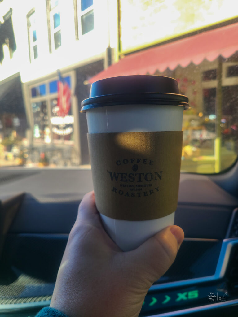 Holding up a to-go coffee cup in front of Weston Coffee Roastery