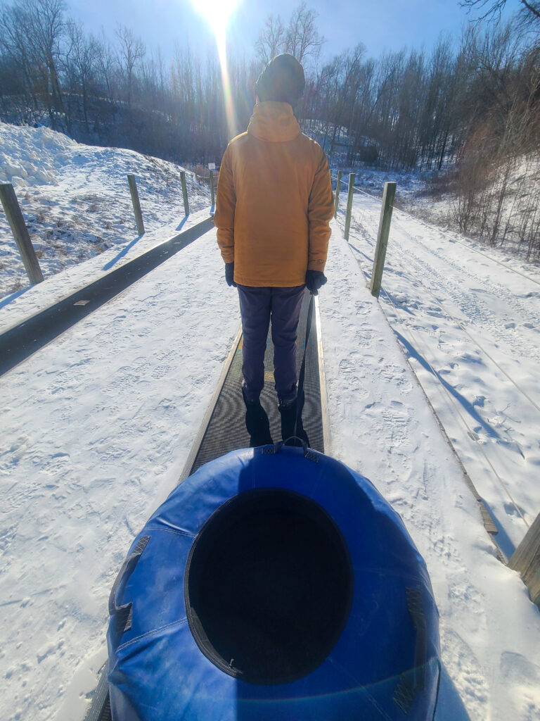 Jason is enjoying his leisurely ride on the moving carpet to the top of the tubing hill, pulling his tube behind him.